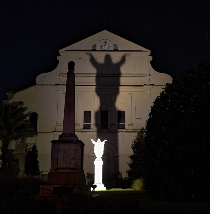 White large face of church with extremely large shadow of jesus with arms open coming from small statue in middle of courtyard, new orleans, NOLA, new orleans photograpghy, travel, travel blog, travel blog new orleans,